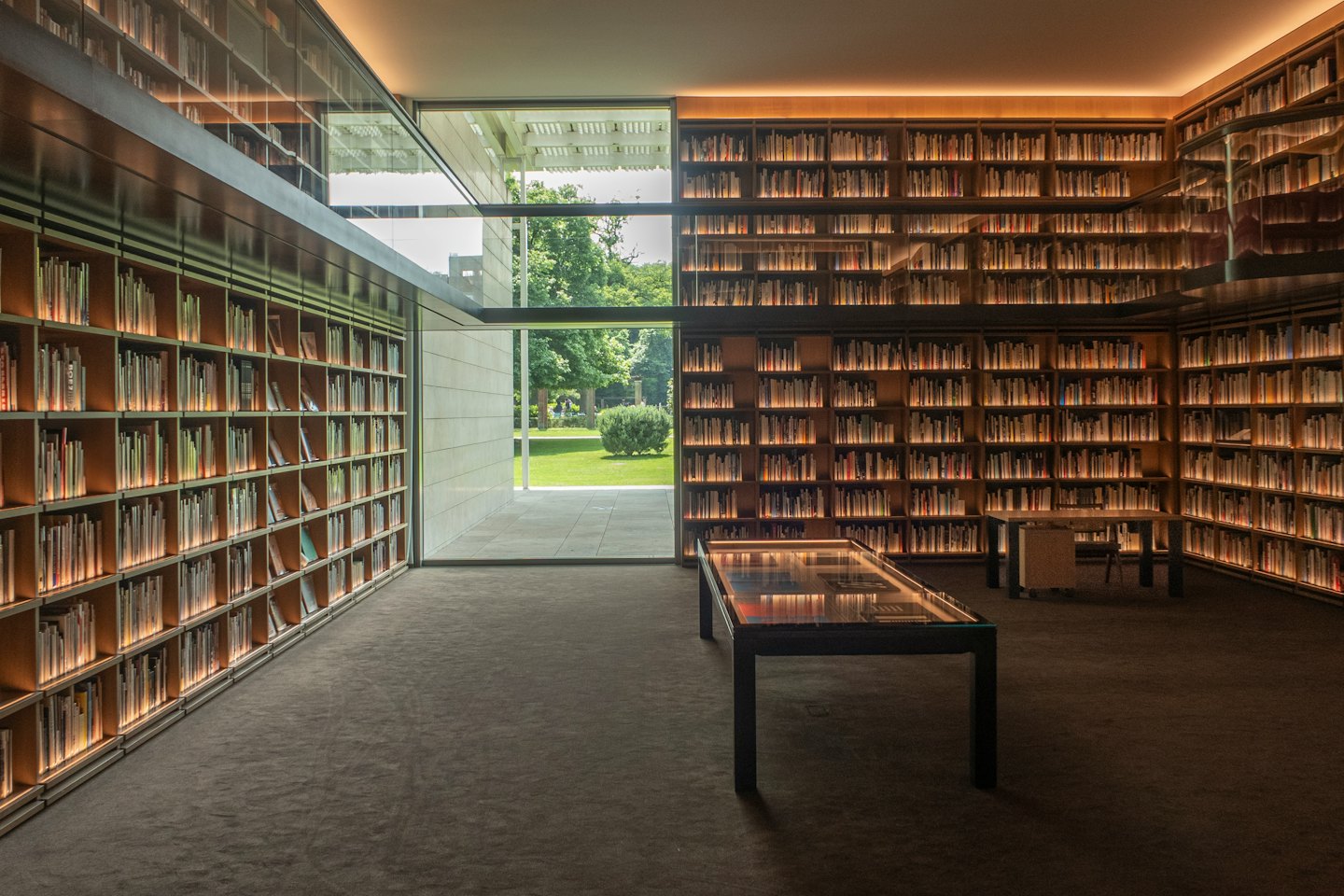 Nowoczesna biblioteka z drewnianymi półkami i szklanymi drzwiami prowadzącymi na trawnik.